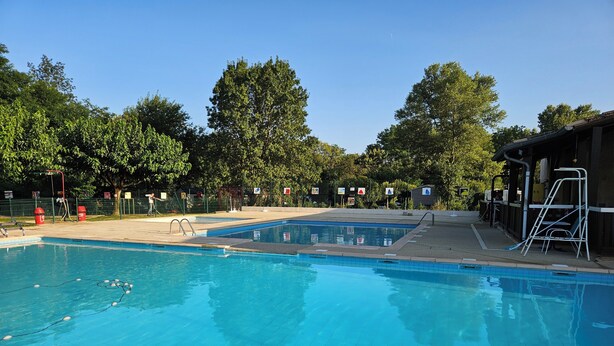 A swimming pool with clear blue water, surrounded by trees and a covered area with a ladder. - Mobile-home Camping L'ardecho [Magnolia] (Saint-Lager-Bressac)