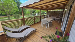 A covered outdoor deck with a table and chairs, a cushioned bench, and a potted plant. - Mobile-home Camping L'ardecho [Magnolia] (Saint-Lager-Bressac)