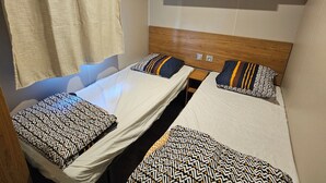 A compact room with two single beds, each with patterned pillows, a wooden headboard, and a small wooden shelf above. - Mobile-home Camping L'ardecho [Magnolia] (Saint-Lager-Bressac)