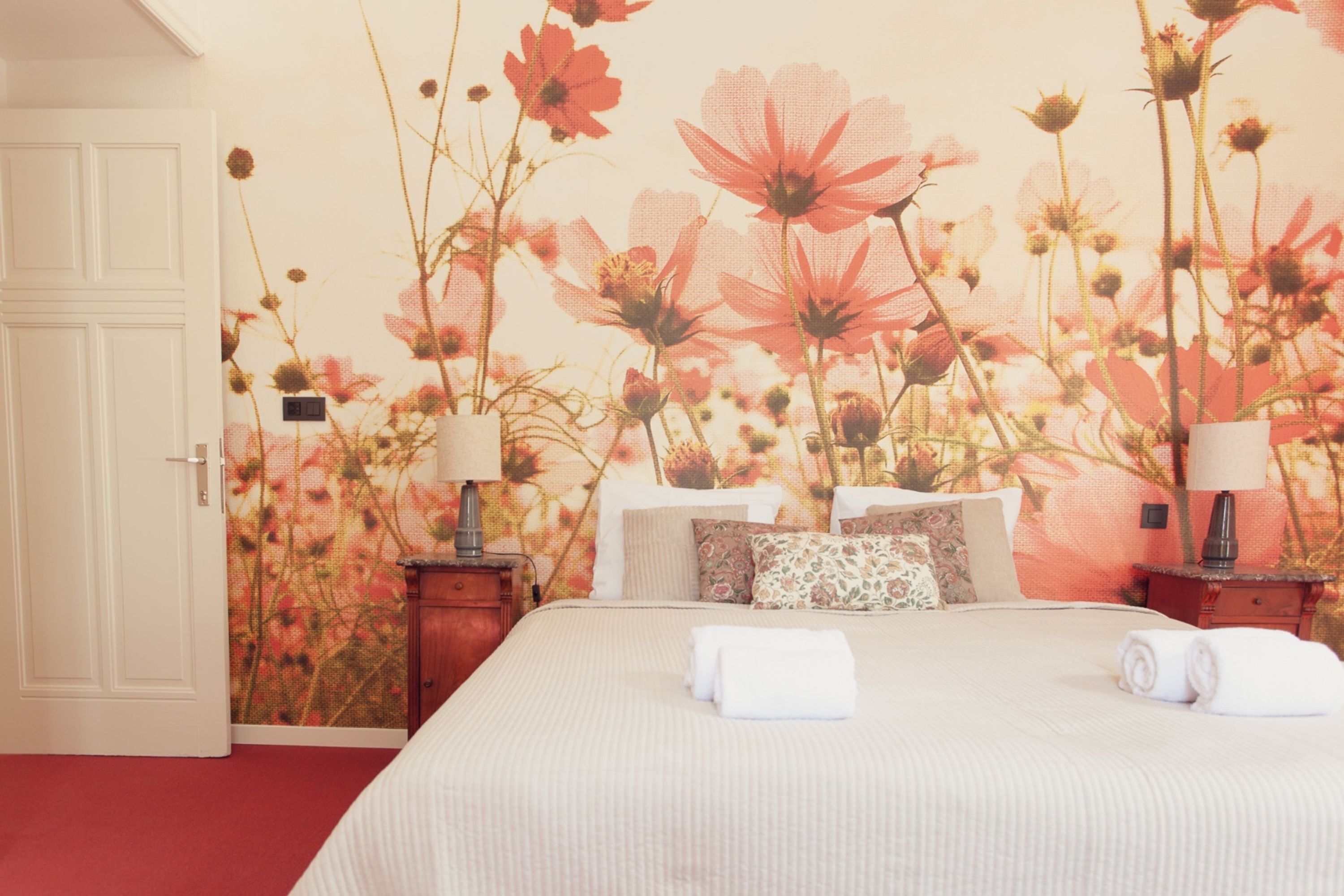 Una camera d'albergo con un letto grande, due comodini con lampade e un affresco floreale al muro.