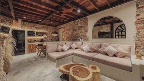 A cozy interior with a stone wall, wooden ceiling beams, a built-in sofa, and a dining area with a wooden table and chairs. - Son's House - La Santisima Cartagena (Cartagena de Indias)