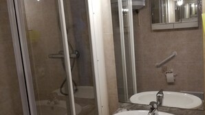 A bathroom with a glass shower enclosure, two sinks, a mirror, and a handrail. - Studio for 2, fully equipped, loggia, park view, city center. (Balaruc-les-Bains)