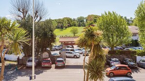 Un área de estacionamiento con coches, un arco de piedra y una vista de un paisaje verde con árboles y una colina al fondo.
