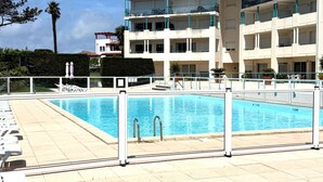 Una piscina con borde de baldosas, rodeada por una valla blanca.