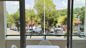 Un balcón con mesa y sillas, con vistas a un aparcamiento con varios coches y un edificio con un cartel.