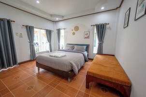 A bedroom with a bed, a wooden bench, and a window with curtains.