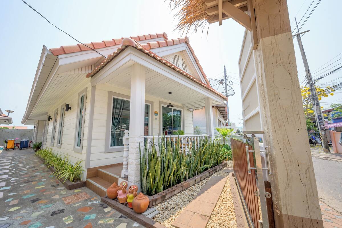 A house with a tiled roof, a porch with a railing, and a pathway leading to the entrance.