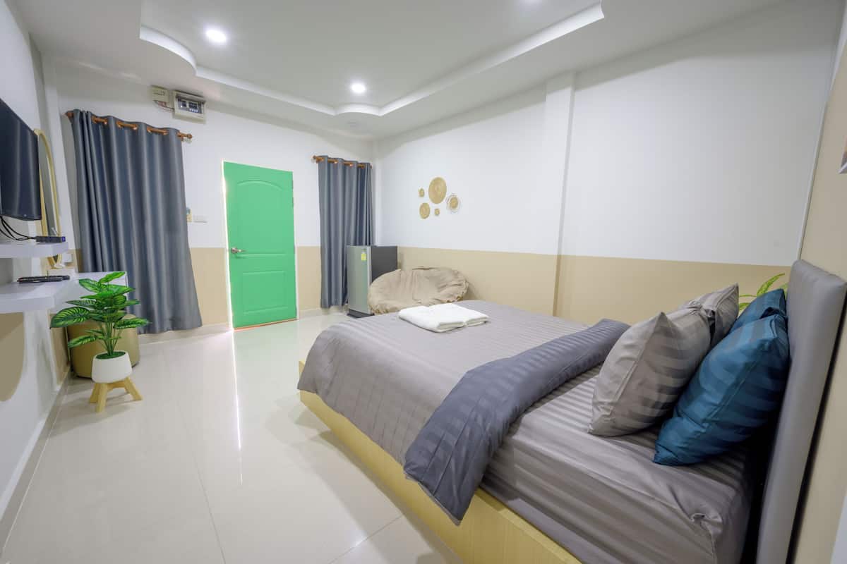 A modern hotel room with a bed, a small desk, a green door, and a potted plant.