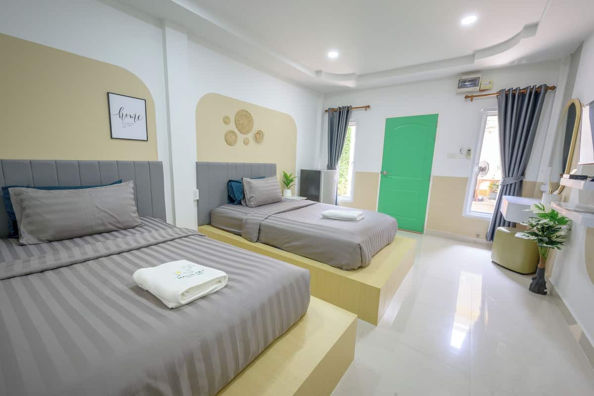 A hotel room with two beds, a green door, a small plant, and a wall-mounted TV.