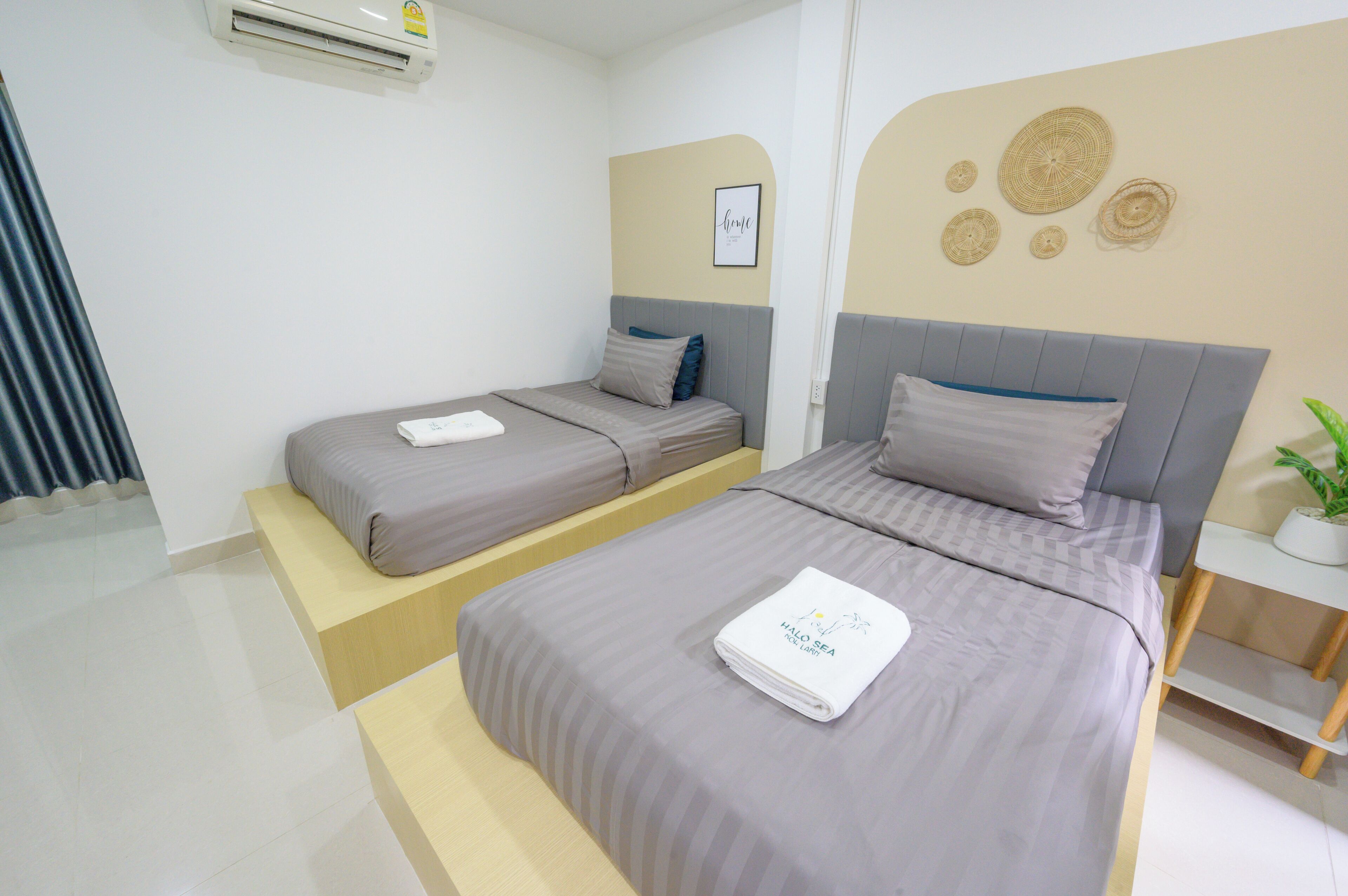 A hotel room with two beds, a small bedside table, and a wall-mounted air conditioner.