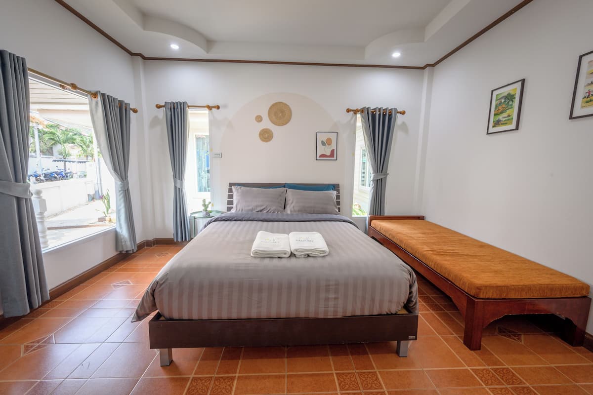A bedroom with a bed, a bench, and a window with curtains.