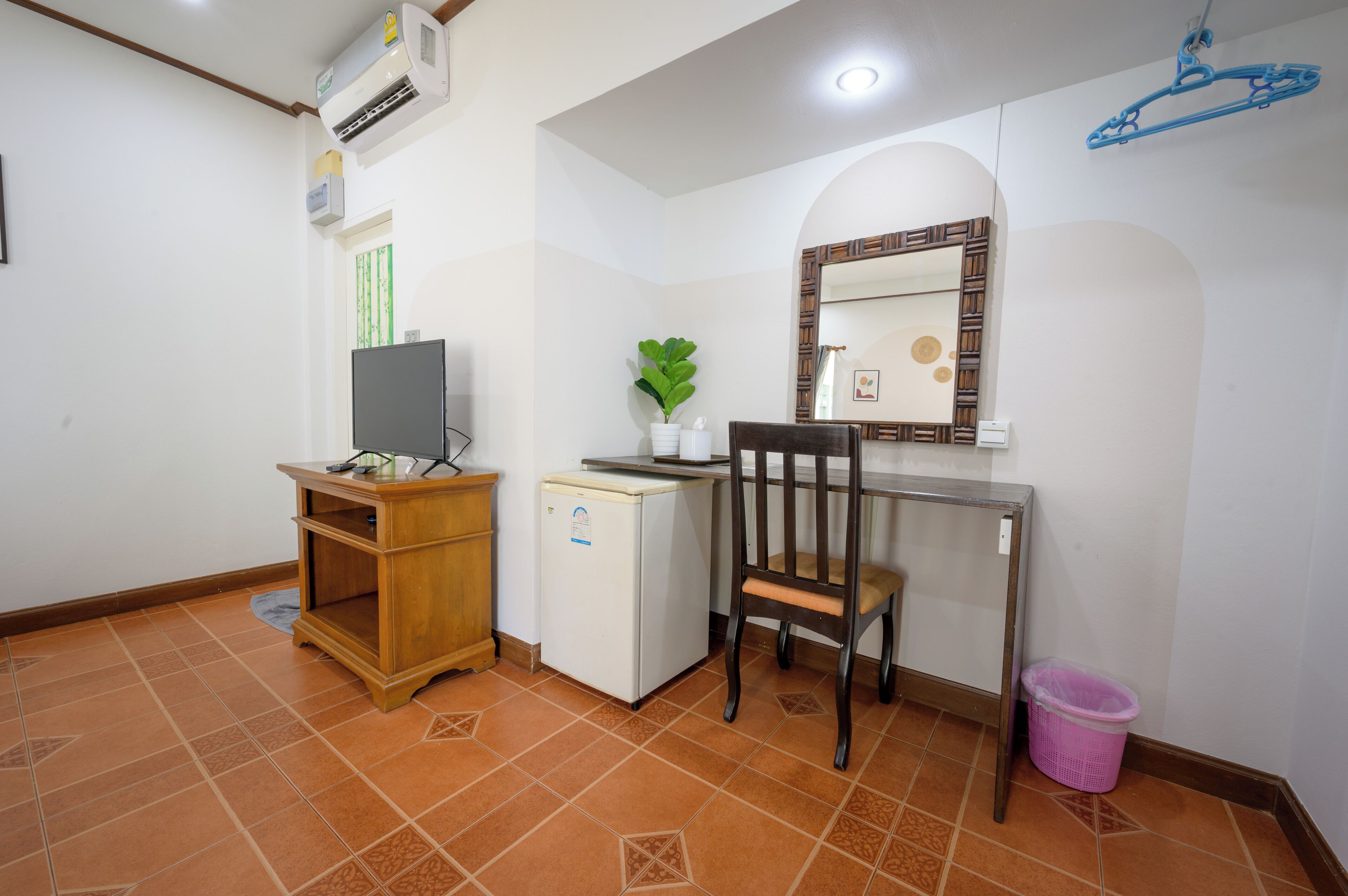 Una oficina pequeña con escritorio, silla, aire acondicionado y un refrigerador pequeño.