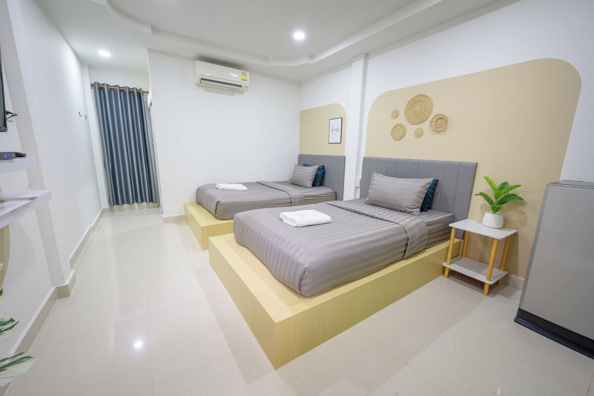A modern hotel room with two beds, a small table, a potted plant, and a wall-mounted air conditioner.