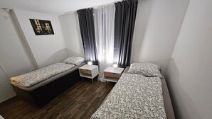 A small, compact room with two single beds, a small table, and a wall-mounted picture. - Apartment 'By B2' with Wi-Fi (Thüngen)