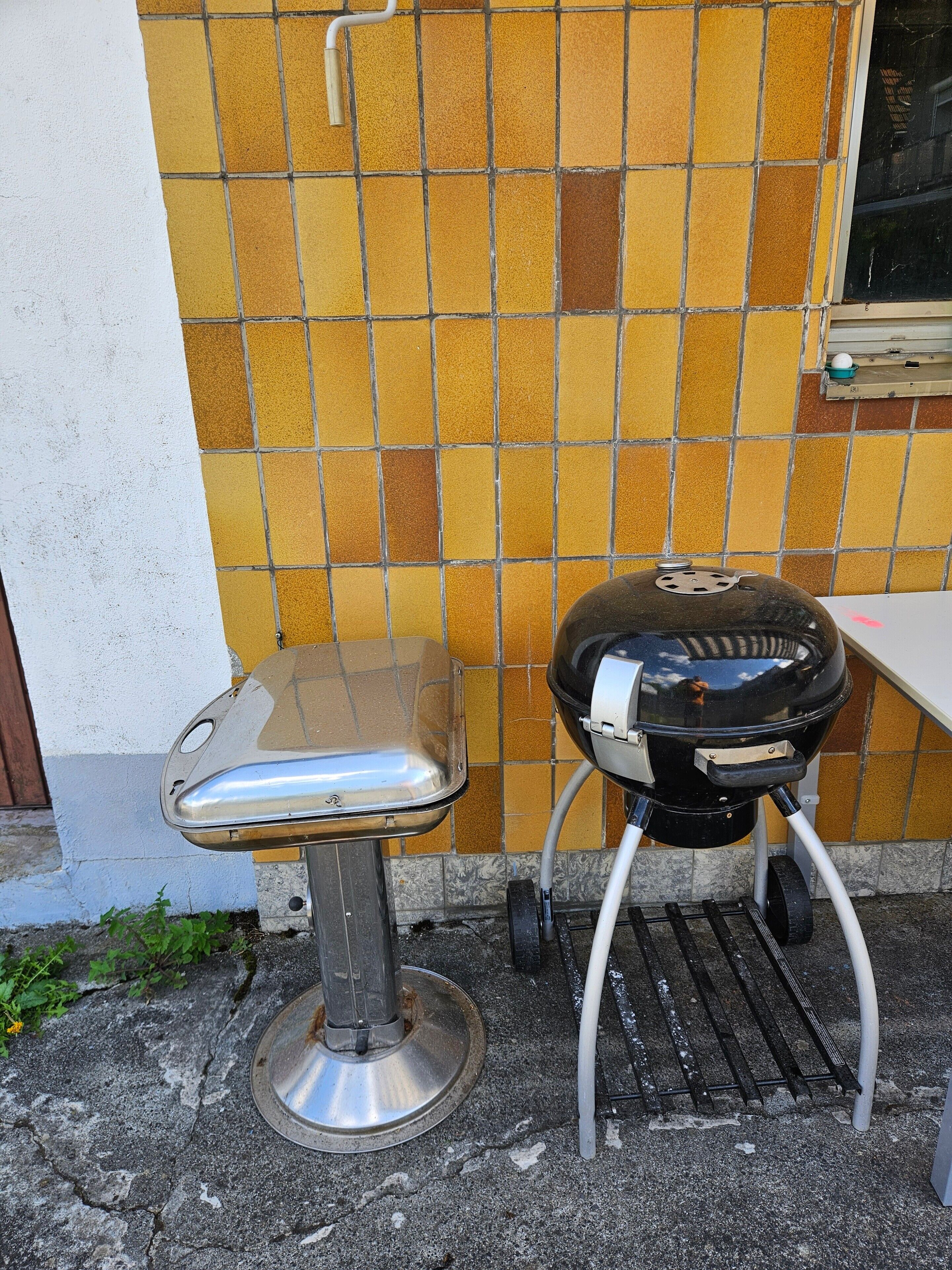 A portable grill with wheels, a metal sink, and a tiled wall with a window.