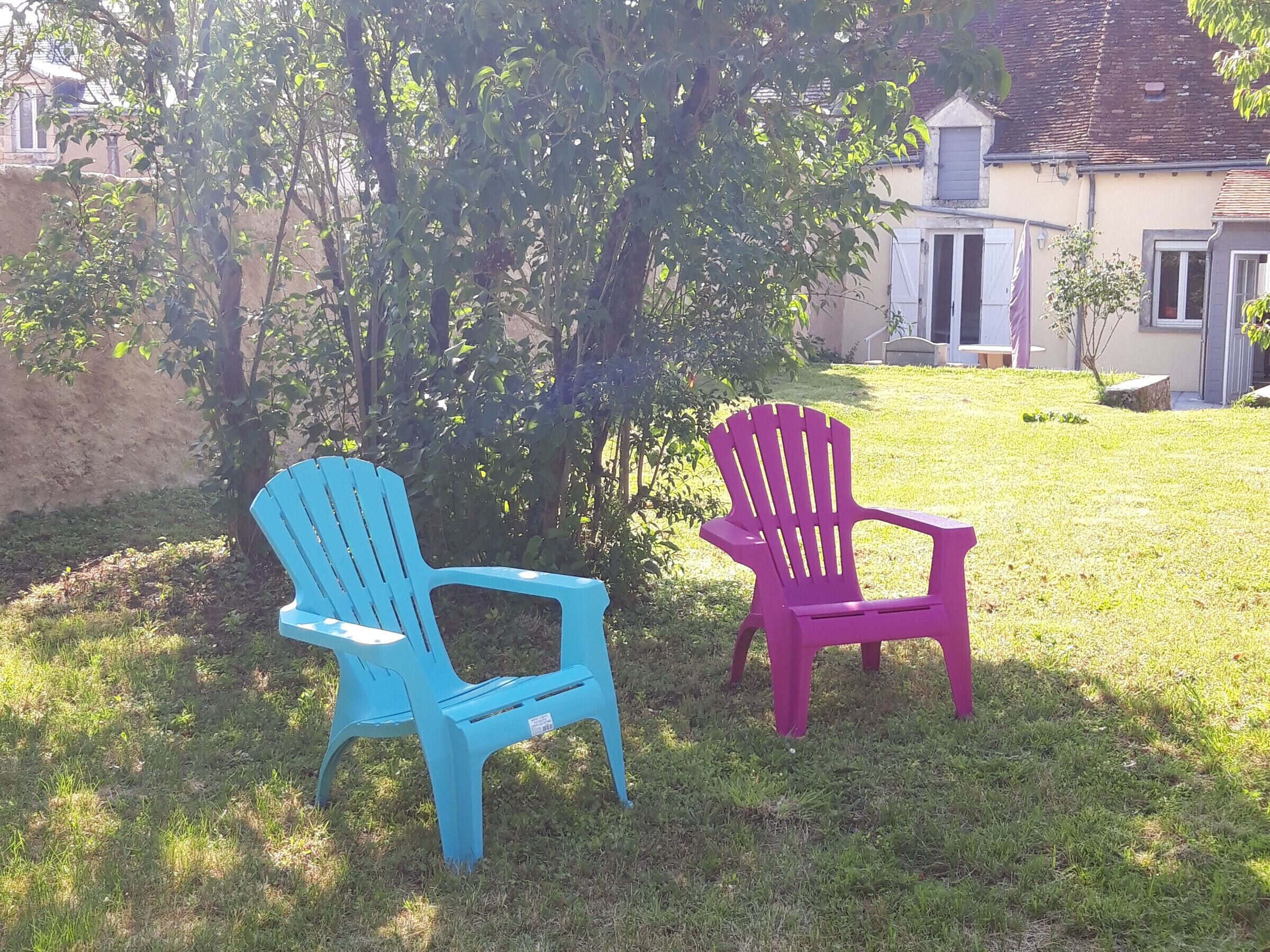 Twee Adirondack stoelen in een gazon met een gebouw op de achtergrond.