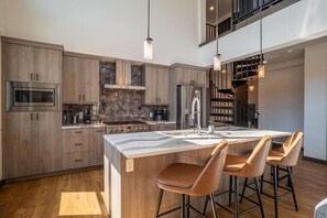 A modern kitchen with a central island, bar stools, and a staircase leading to an upper level.