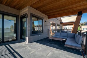 Un patio exterior moderno con techo de madera, grandes puertas correderas de vidrio y un sofá empotrado.