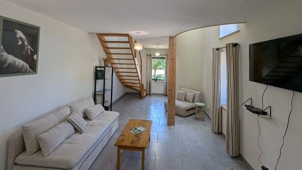 A modern living room with a wooden staircase, a sofa, a coffee table, and a TV mounted on the wall. - Gîte le Saule between Épinal and Saint-Dié with Wi-Fi (Nonzeville)
