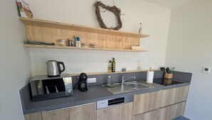 A modern kitchen with a built-in microwave, coffee maker, and sink. There are wooden shelves above the counter holding various items. - Gîte le Saule between Épinal and Saint-Dié with Wi-Fi (Nonzeville)