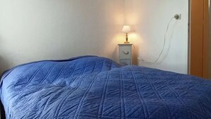 A bedroom with a bed, a nightstand with a lamp, a wall-mounted picture, and a wooden door. - 50m² House near beach in Le Croisic with parking (Le Croisic)