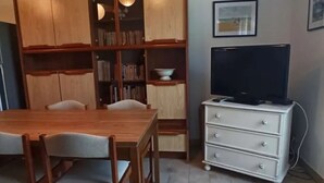 A dining area with a wooden table and chairs, a bookshelf, a television on a cabinet, and a tiled floor. - 50m² House near beach in Le Croisic with parking (Le Croisic)