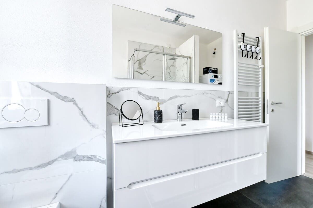 Une salle de bain moderne avec un meuble-lavabo en marbre blanc, un grand miroir, un porte-serviettes et un espace douche.