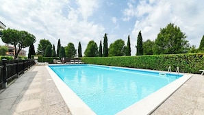 Ein rechteckiger Pool mit Fliesen umrandet, umgeben von einer Hecke und Bäumen.