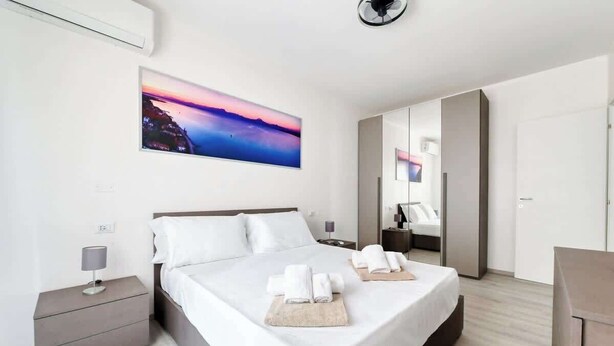 Ein modernes Hotelzimmer mit einem großen Bett, einem Nachttisch, einer Nachttischlampe, einem Sonnenuntergangsgemälde und einem Kleiderschrank.