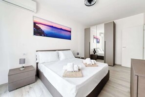 A modern hotel room with a large bed, a nightstand, a bedside lamp, a painting of a sunset, and a wardrobe. - Golden House - Vacations in Sirmione (Sirmione)