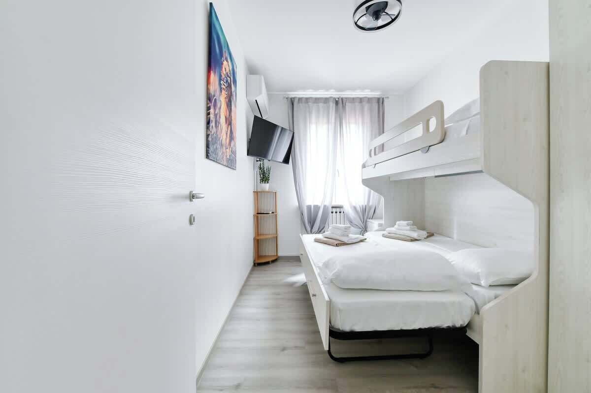 Ett modernt, minimalistiskt hotellrum med en våningssäng, en platt-TV, en tavla på väggen och ett fönster med gardiner.