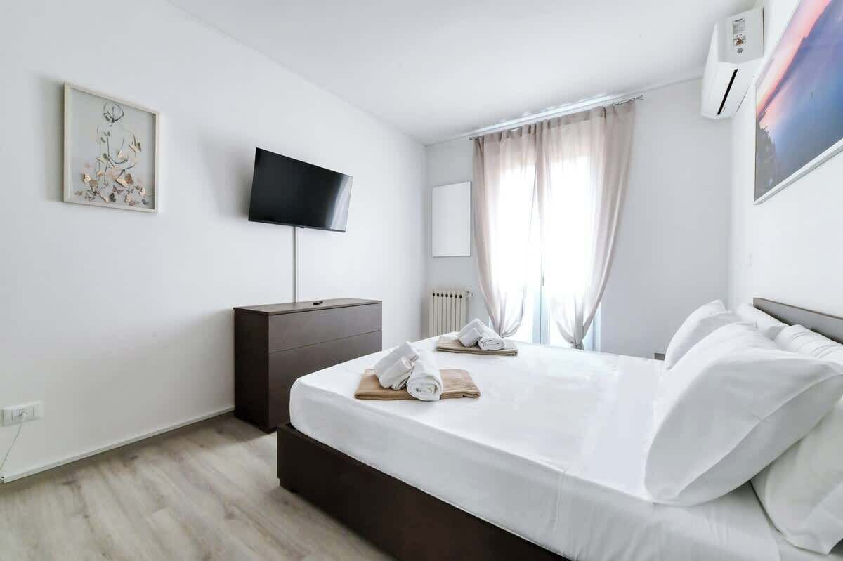 Ein modernes Hotelzimmer mit einem großen Bett, einem flachbildfernseher an der Wand, einem Nachttisch und einem Fenster mit Vorhängen.
