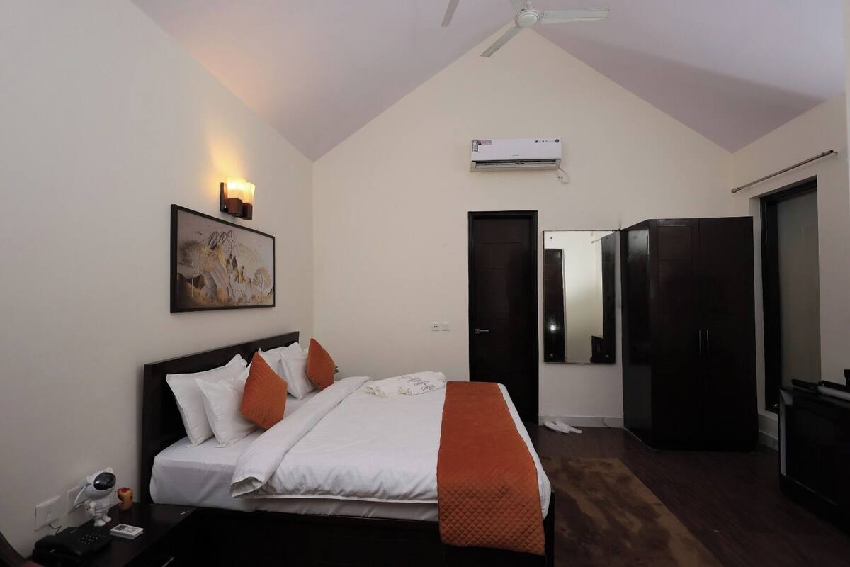 A bedroom with a bed, a nightstand, a desk, a chair, a wardrobe, a ceiling fan, an air conditioning unit, and a door.