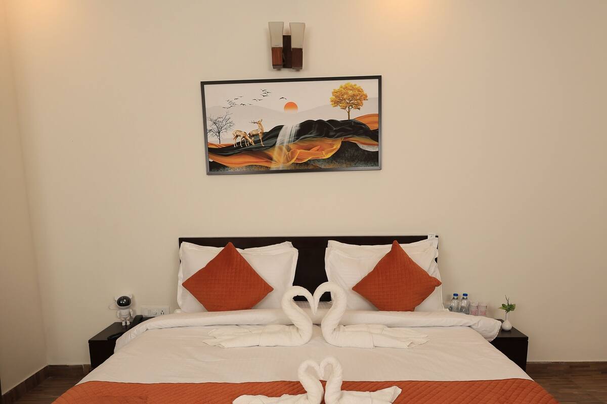 A neatly made bed with white and orange bedding, a framed picture above it, and a swan-shaped towel arrangement on the bed.