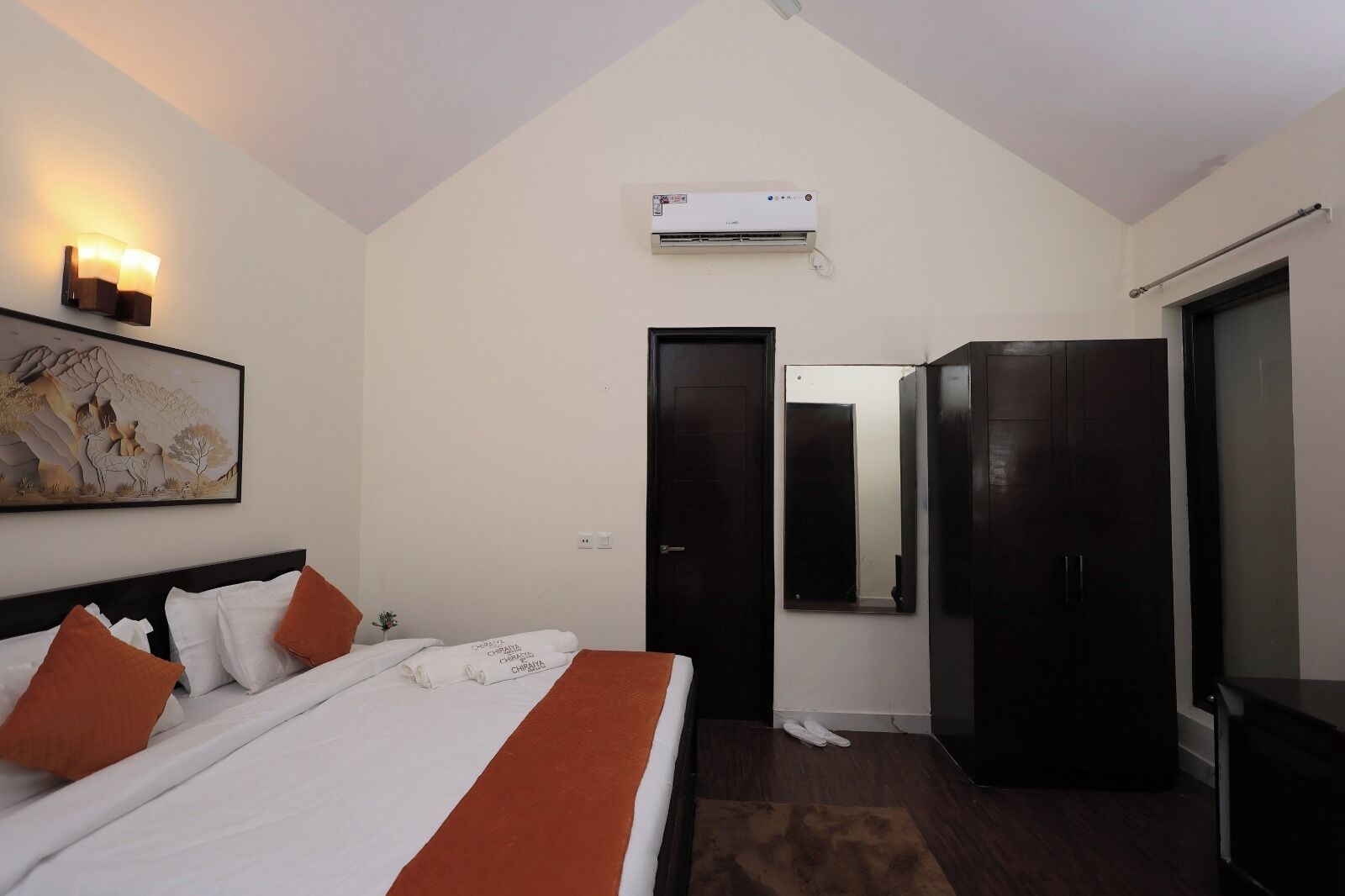A bedroom with a bed, a wall-mounted air conditioner, a door, a mirror, and a painting.