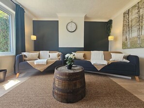 Un salon avec deux canapés, une table basse ronde en bois, une horloge murale et un tableau.