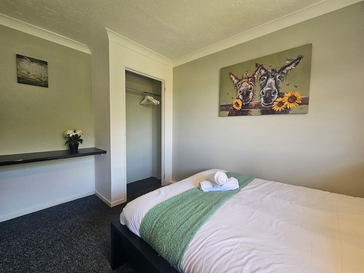 Ein Schlafzimmer mit einem Bett, einer grünen Tagesdecke, einem Gemälde von Eseln und einer kleinen Pflanze.