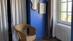 Una habitación con pared azul, una silla de mimbre, un radiador blanco y una ventana con cortinas.