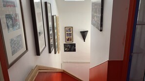 Una escalera con paredes rojas y un tragaluz. Se observan obras de arte enmarcadas en las paredes.