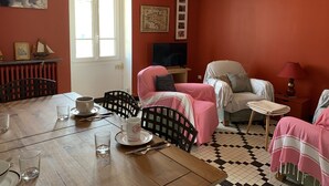 Una habitación acogedora con una mesa de comedor de madera dispuesta para dos, un televisor y una ventana con cortinas.