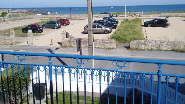 Ein Parkplatz mit mehreren Autos, einer Steinmauer und Blick auf das Meer.