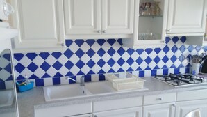 Eine Küche mit weißen Schränken, einer Rückwand mit blau-weißem Rautenmuster, einem Gasherd und einer Spüle.