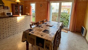 Comedor con una mesa cubierta por un mantel estampado, una pared de ladrillo, un microondas y vistas a zonas verdes a través de una puerta corredera.