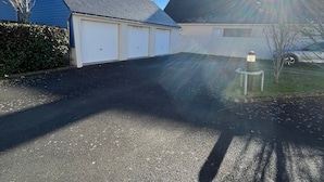 Una strada privata residenziale con un garage, un siepe e un'auto parcheggiata.