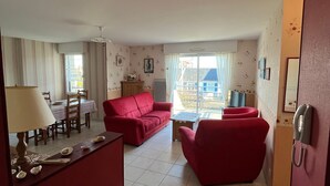 Un soggiorno con un divano rosso, un tavolo da pranzo con sedie, una lampada e vista all'esterno.
