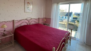 Una camera da letto con un letto, un comodino, una lampada, un quadro appeso e vista all'esterno da una finestra.