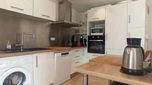 Een kleine keuken met een wasmachine, een magnetron, een koffiezetapparaat en een waterkoker.