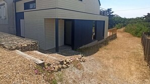 Een twee verdiepingen tellend huis met een schuin dak, een veranda en een grindpad.