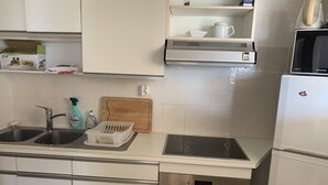 Une cuisine équipée d’un évier à deux bacs, d’un four à micro-ondes, d’un réfrigérateur et d’une planche à découper en bois posée sur le plan de travail.