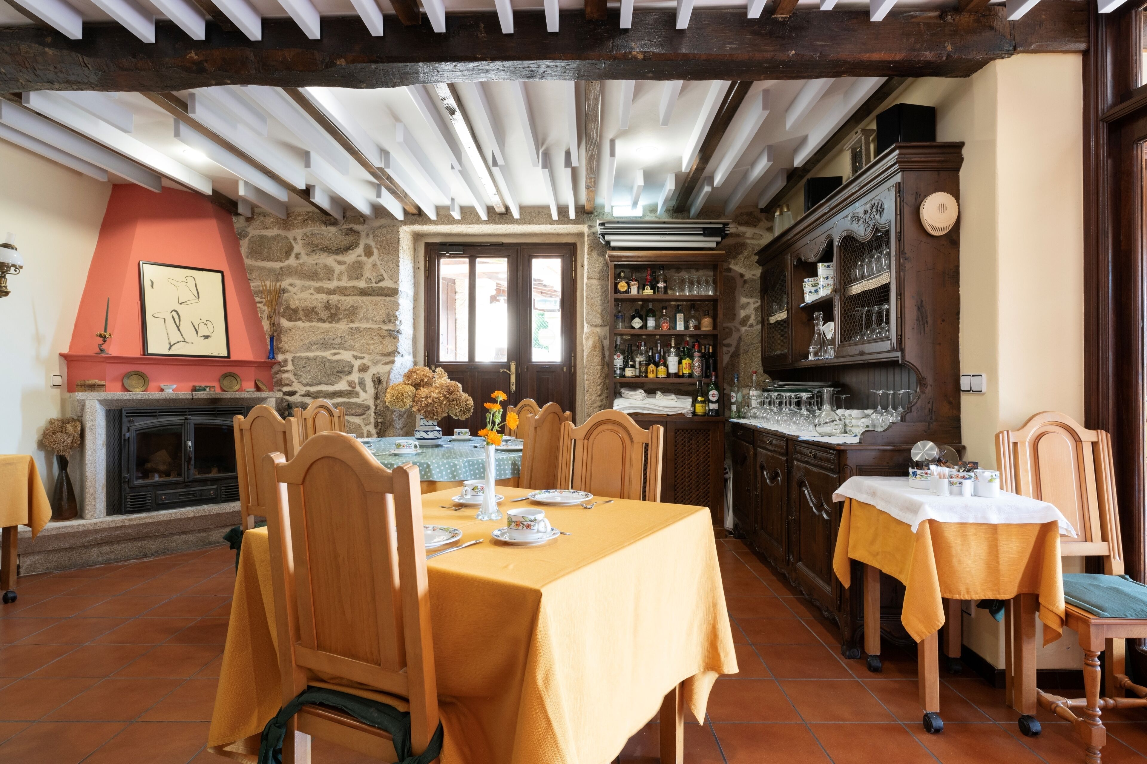 Un espace repas avec des tables et des chaises en bois, une cheminée en pierre et un bar avec des étagères remplies de bouteilles et de verres.